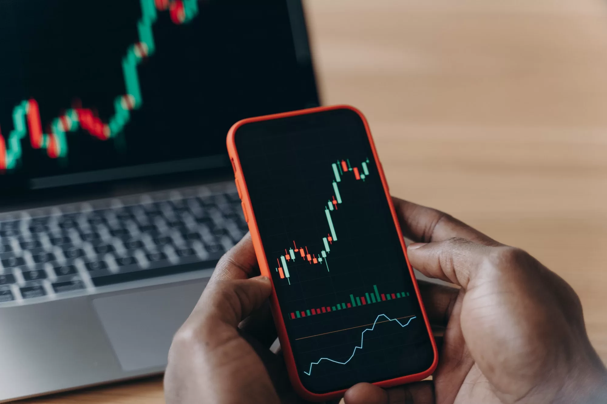 The Ultimate Guide to Learning Day Trading: Tips from a Successful Trader Male hands of African man holds smartphone in front of laptop with trading charts on it