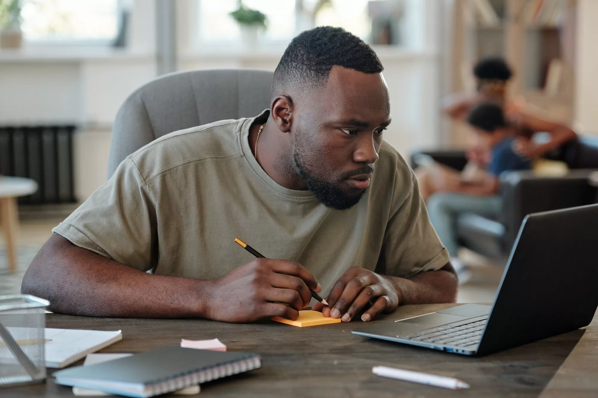 Young African man with pencil over notepaper sitting by table in front of laptop. How to use the UNAM Moodle Login
