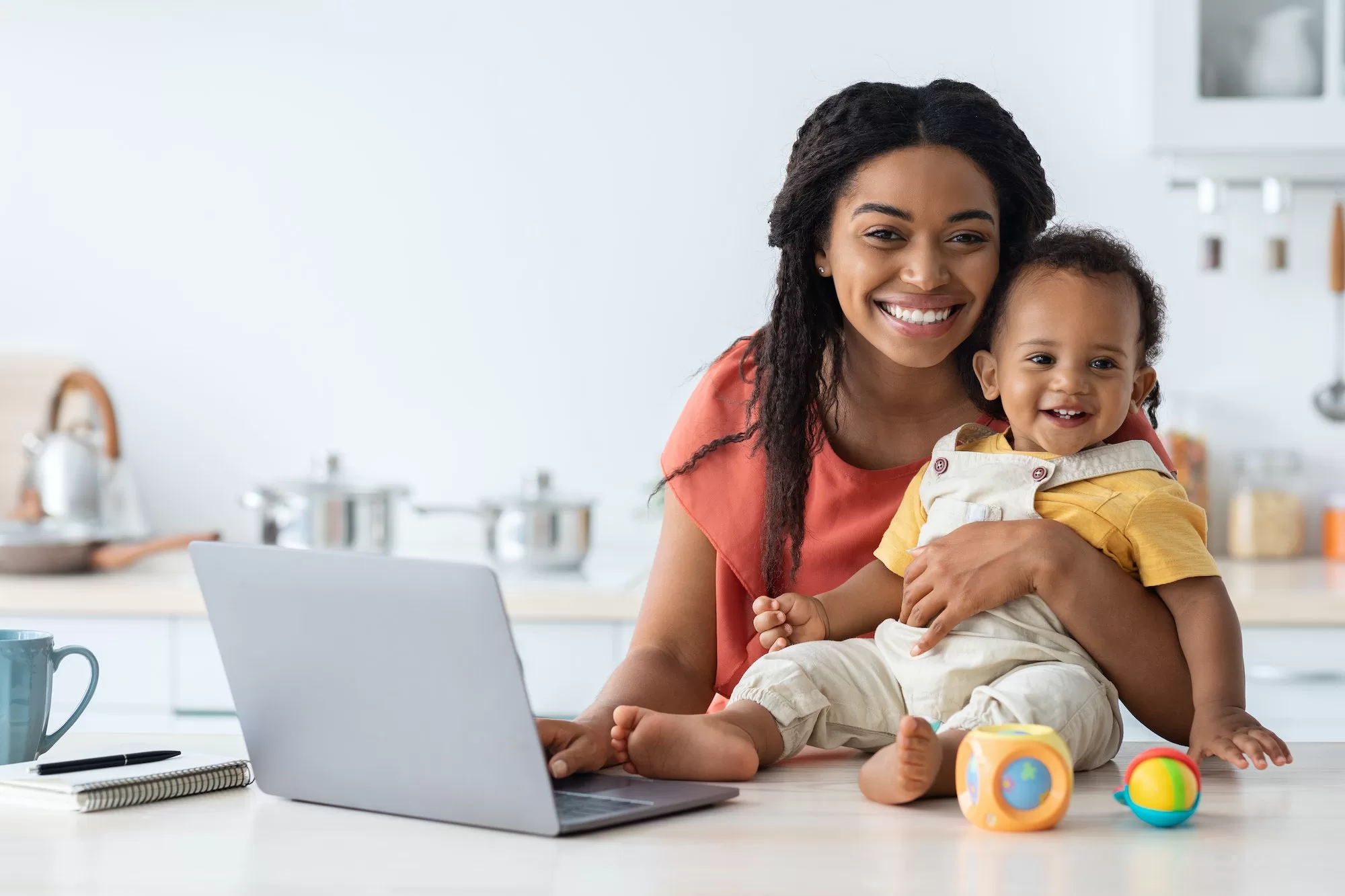 Happy Maternity Leave. Black Lady Working On Laptop With Baby In Kitchen | Submission of Documents for Maternity Leave Benefits Claim