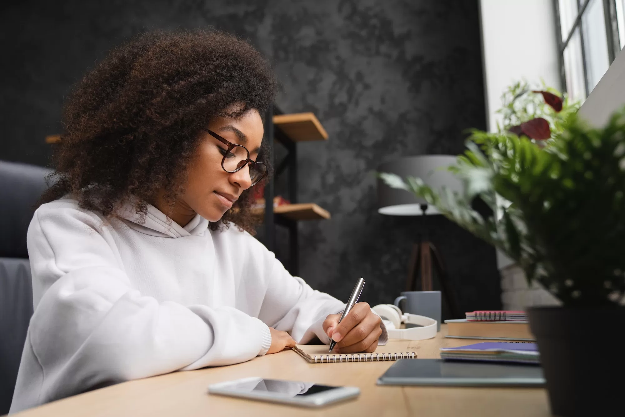 NMH Bursary Student doing homework, writing in copybook using smartphone. E-learning. Homeschool.