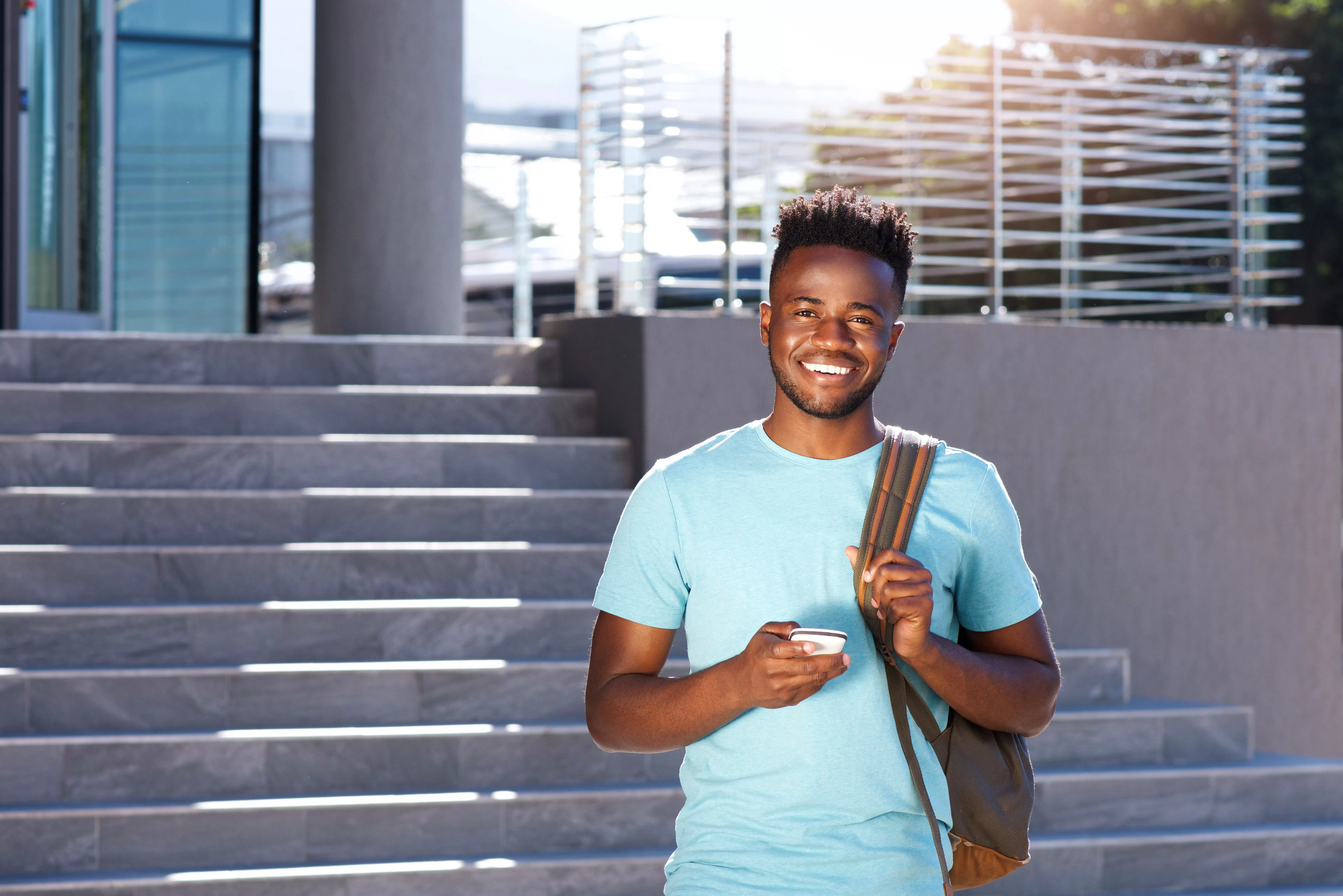 smiling african student walking by stairs with bag and smart phone. Namibian Academy for Tourism and Hospitality (NATH): Your Odyssey into Hospitality Finesse